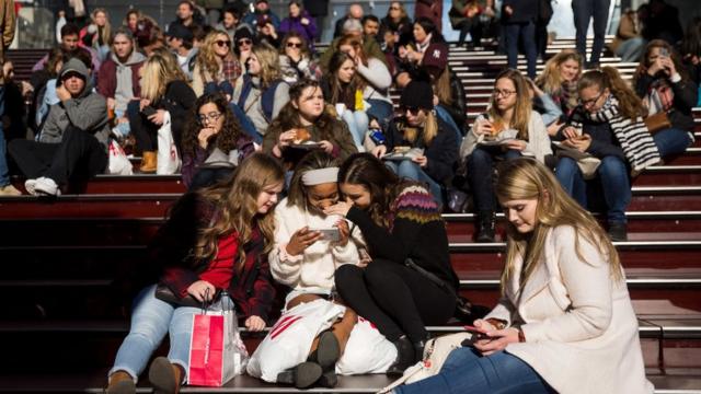 A group of teens look at a photograph they took on a smartphone in Times Square in New York City